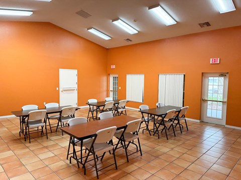 A room with orange walls and tiled floors has tables and chairs set up.