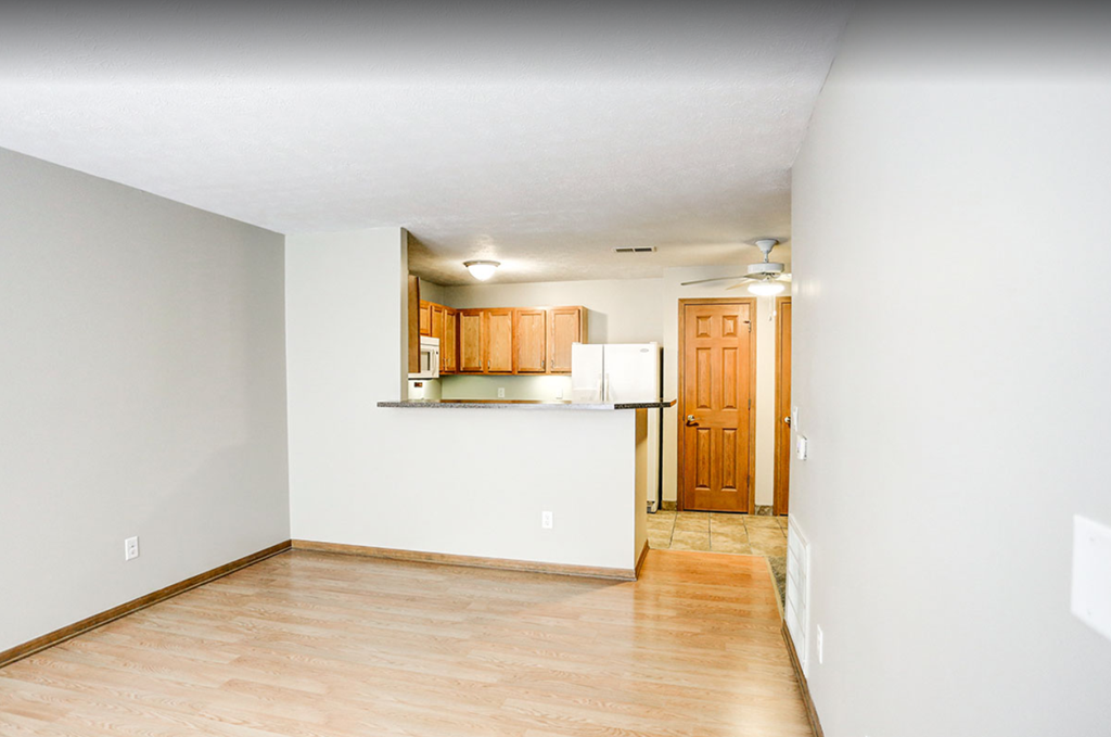 an empty living room and kitchen with wood floors and white walls