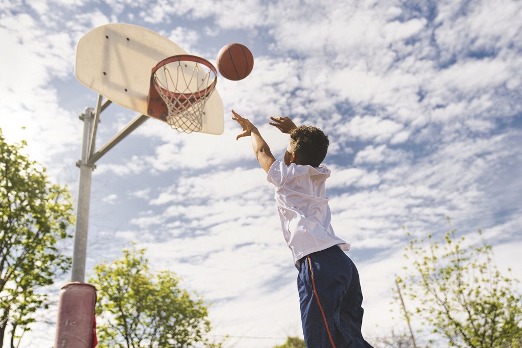 A boy in a white shirt and blue shorts is shooting a basketball into a hoop.