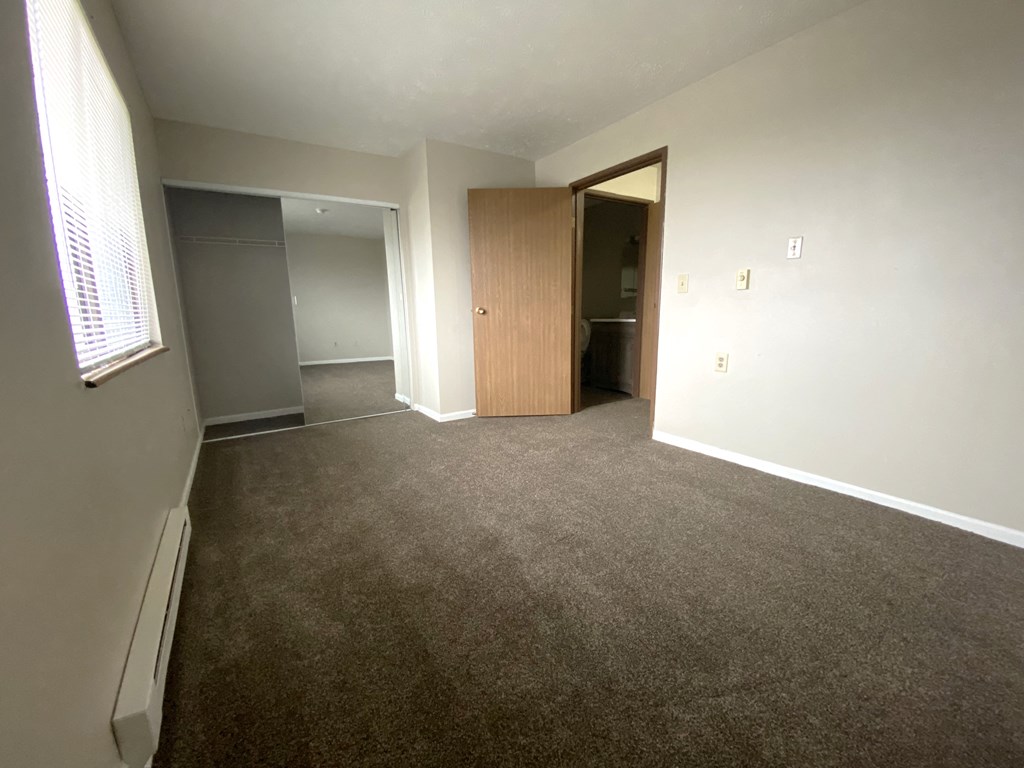 an empty living room with carpet and a door into a bedroom