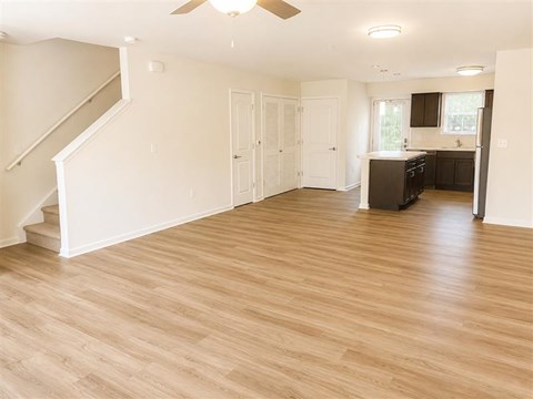 A spacious room with wooden flooring and a staircase on the left side.