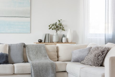 A white couch with grey pillows and a grey blanket.