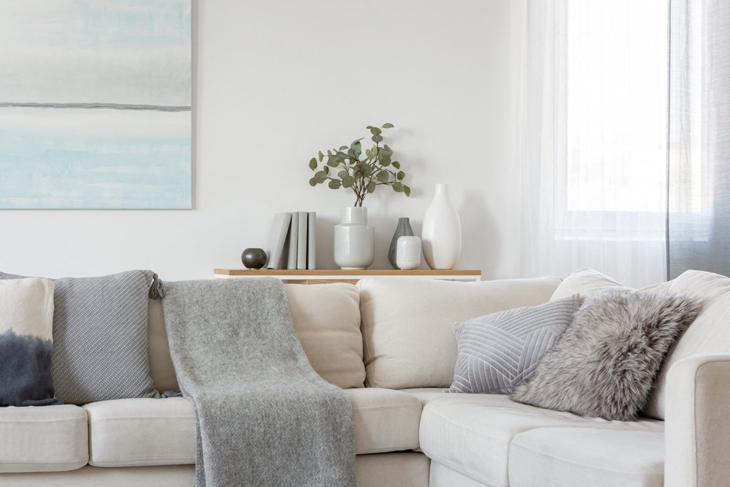 A white couch with grey pillows and a grey blanket.
