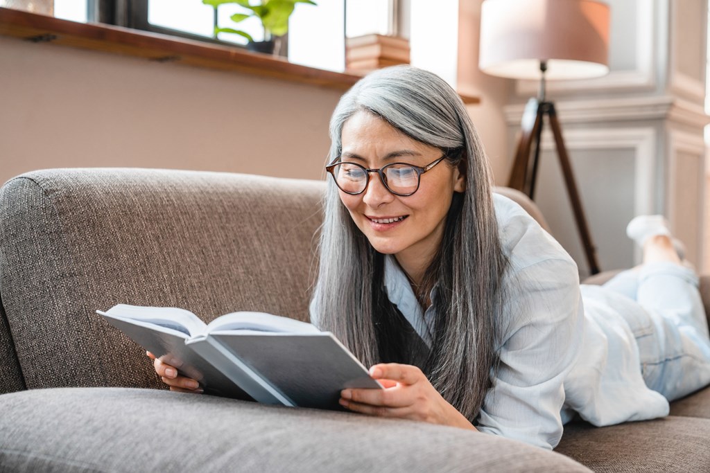 A person is reading a book on a grey couch.