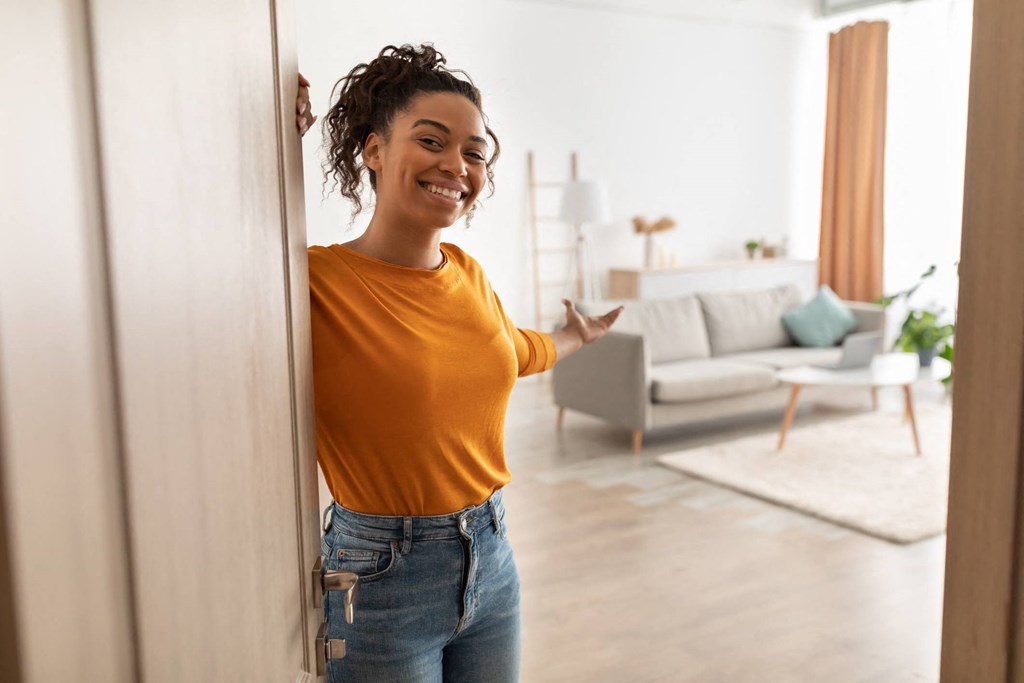 A woman in a yellow top and blue jeans stands in a room with a couch and a rug.