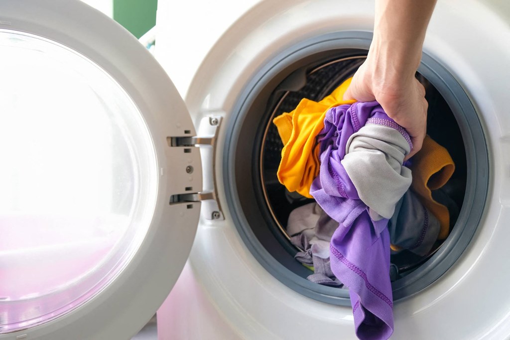 A person is loading clothes into a washing machine.