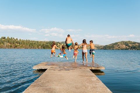 A group of people jumping into a lake from a concrete pier.