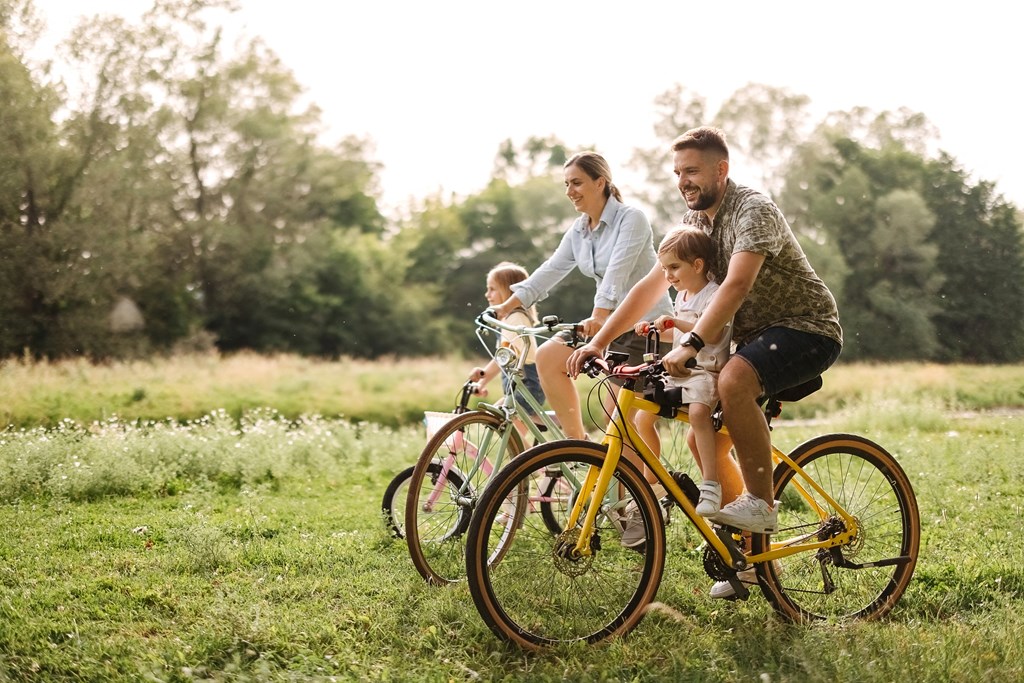 A family of three is riding a bicycle together in a field.
