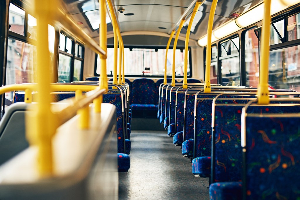 The interior of a bus with rows of seats and yellow poles.