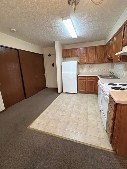 A kitchen with a white refrigerator and brown cabinets.
