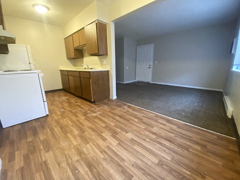 an empty living room with a kitchen and wood flooring