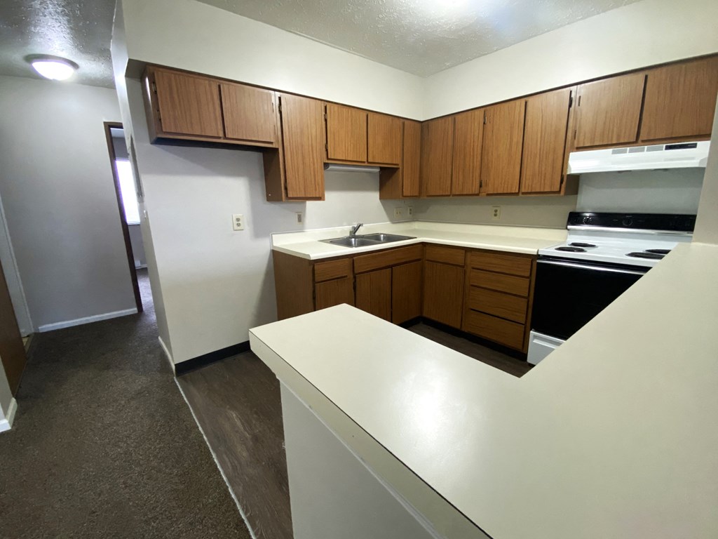 an empty kitchen with white countertops and wooden cabinets