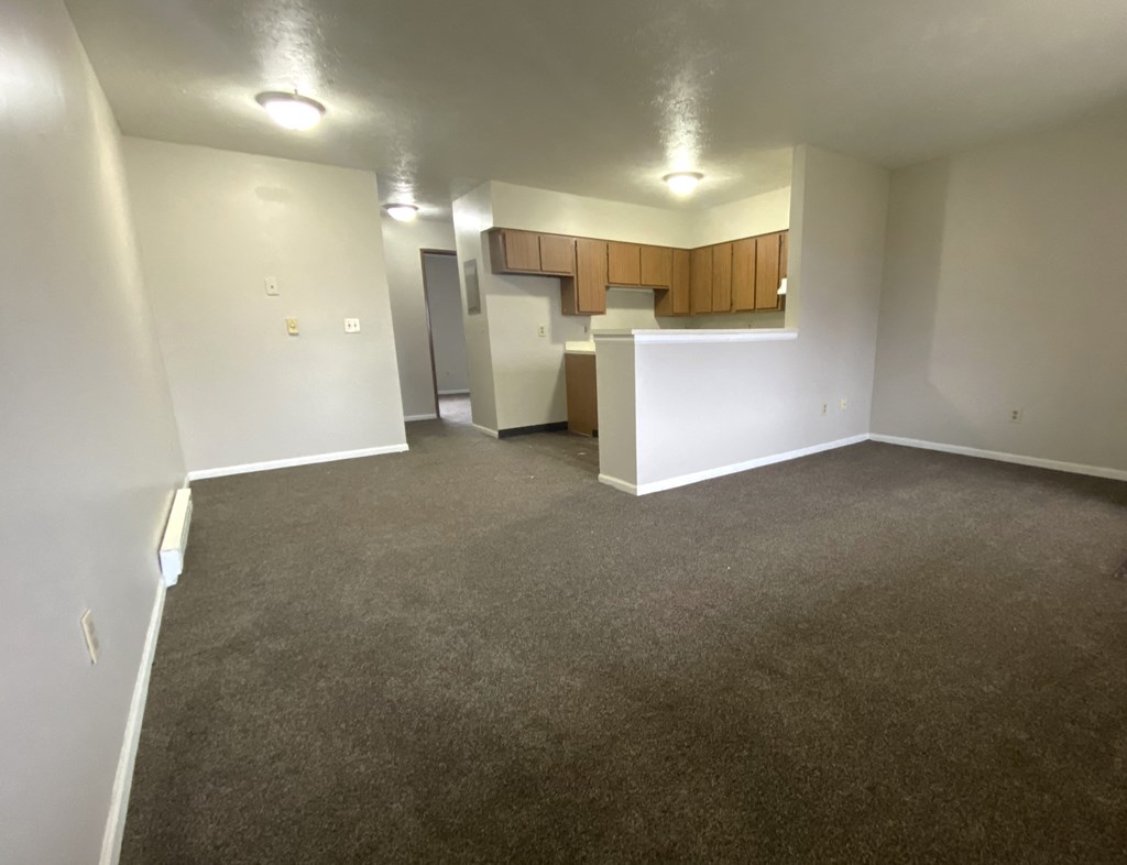 an empty living room with a kitchen in the background