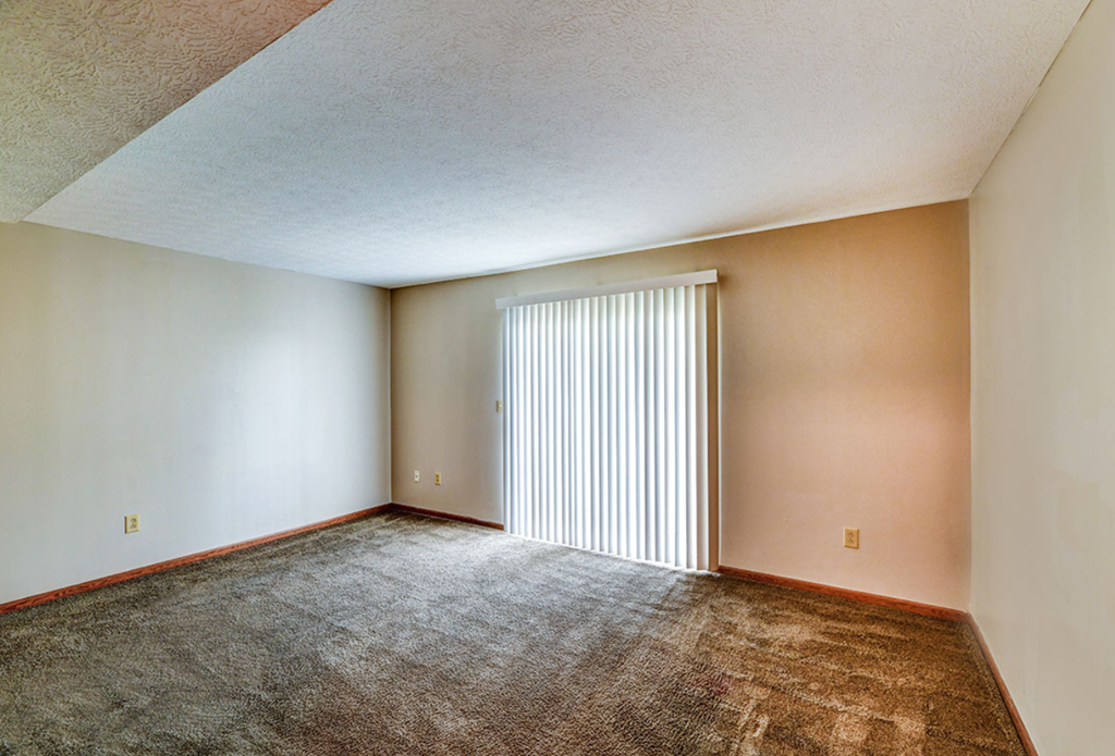 an empty living room with a large window with blinds