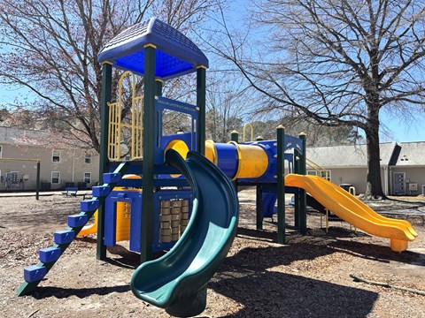 A playground with a blue and yellow slide and a green slide.