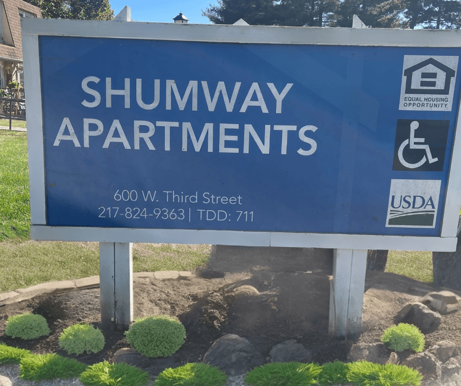 a blue sign that says in front of a yard with plants