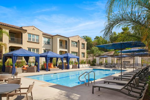 A swimming pool area with lounge chairs and umbrellas in front of apartment buildings.