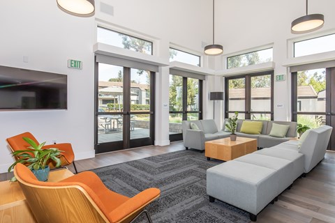 A modern waiting room with a grey sofa, orange chairs and a TV on the wall.