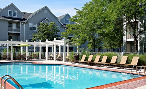 A pool surrounded by chairs and trees in front of apartment buildings.