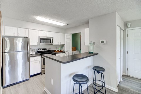 A kitchen with a refrigerator, microwave, oven, and a counter with two stools.