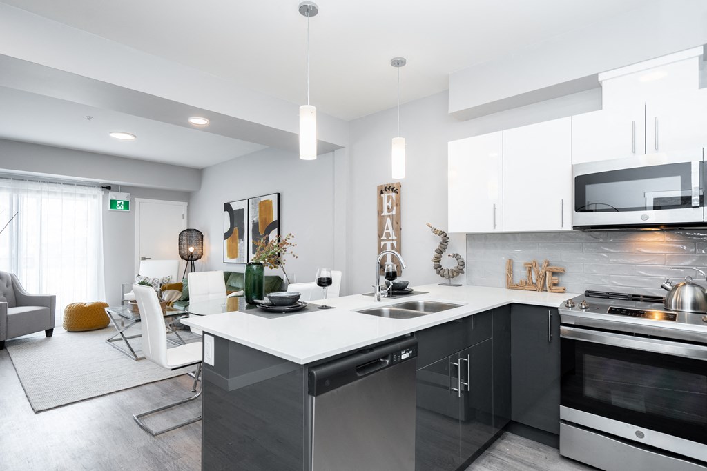 a kitchen with white countertops and dark cabinets with a living room in the background