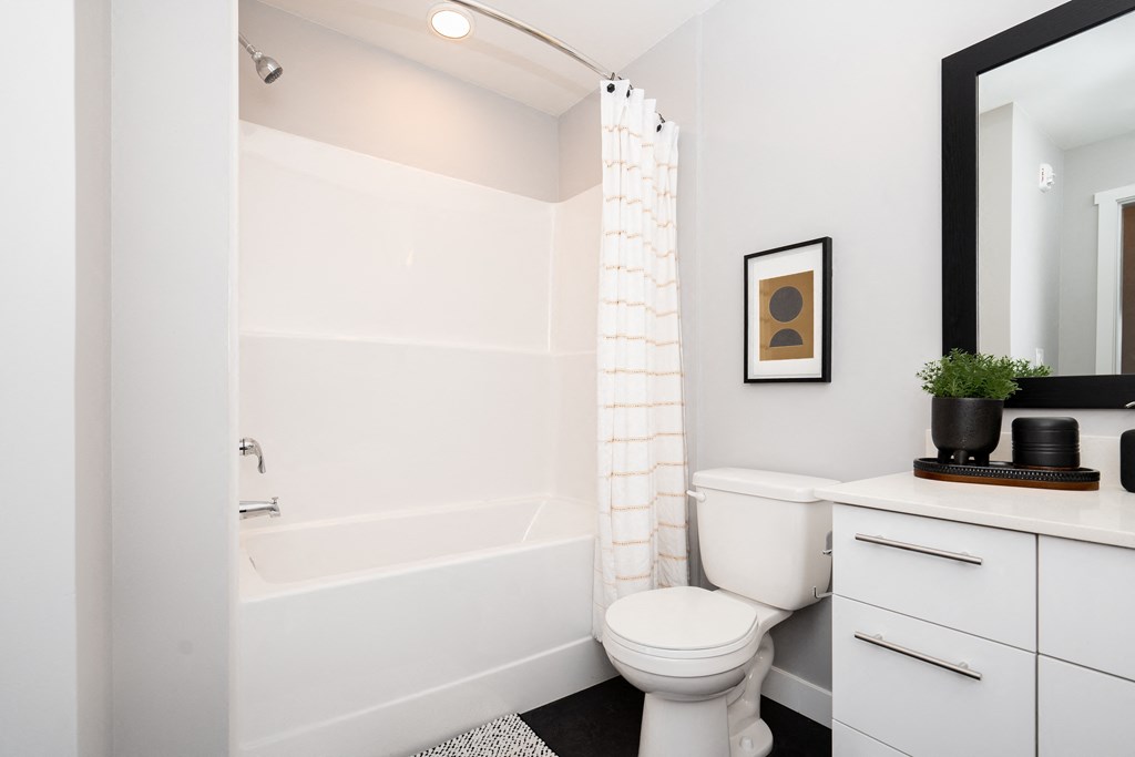 a bathroom with white walls and a white toilet next to a white bathtub