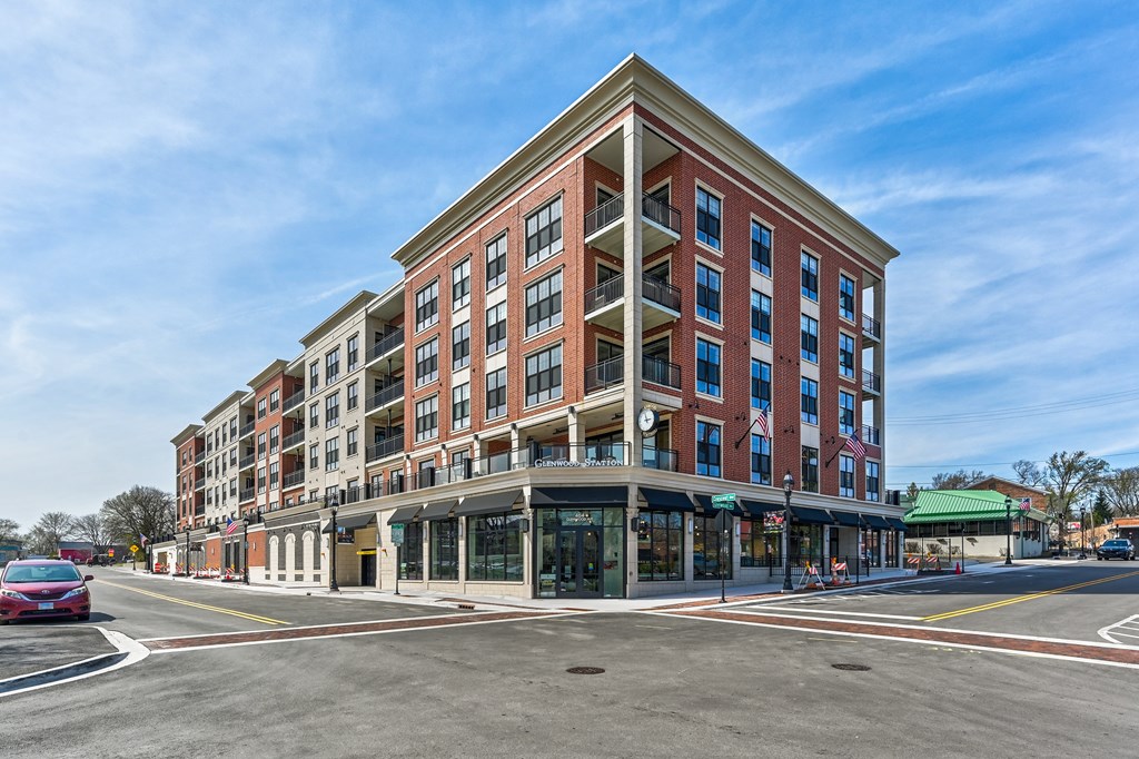 A red car is parked on the side of the road in front of a multi-story building.