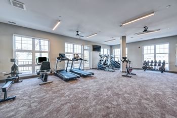 A spacious gym with a variety of exercise equipment and large windows.