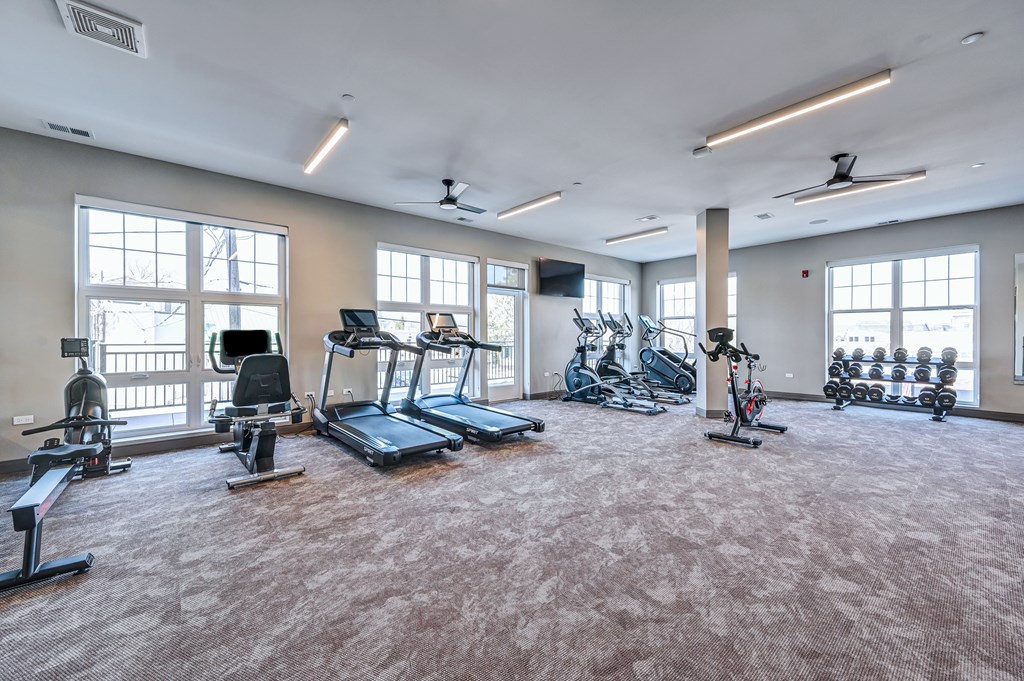 A spacious gym with a variety of exercise equipment and large windows.