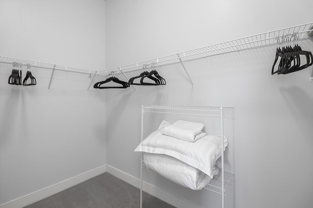 A white closet with clothes hanging and towels on a shelf.