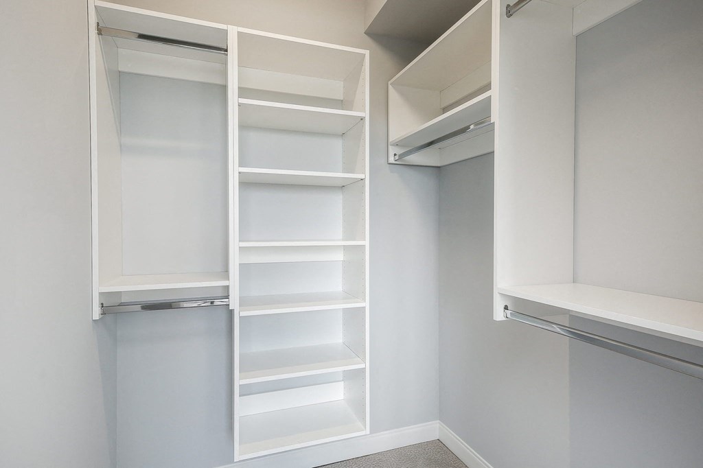 a walk in closet with white shelving and empty shelves