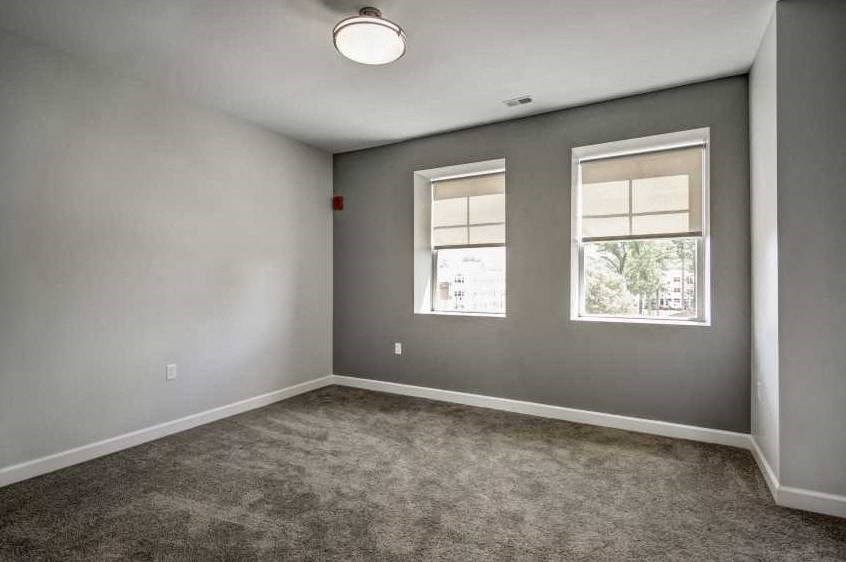 an empty living room with two windows and a carpet