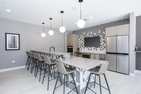 a kitchen with a long island with bar stools and a stainless steel refrigerator