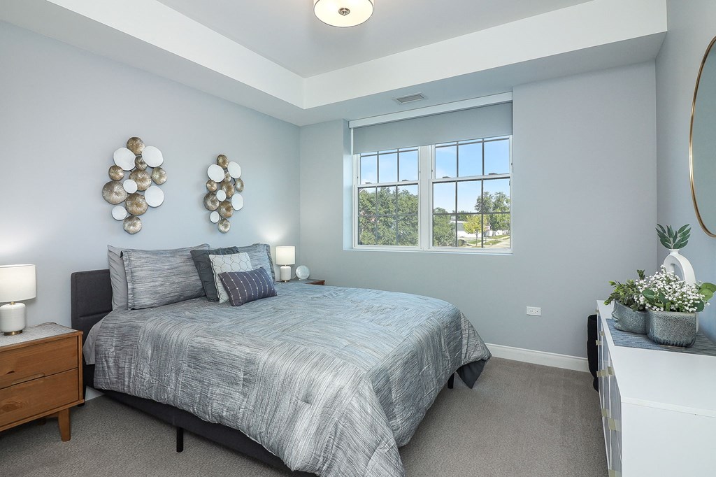 A bedroom with a bed, nightstand, and a window with a view of trees.
