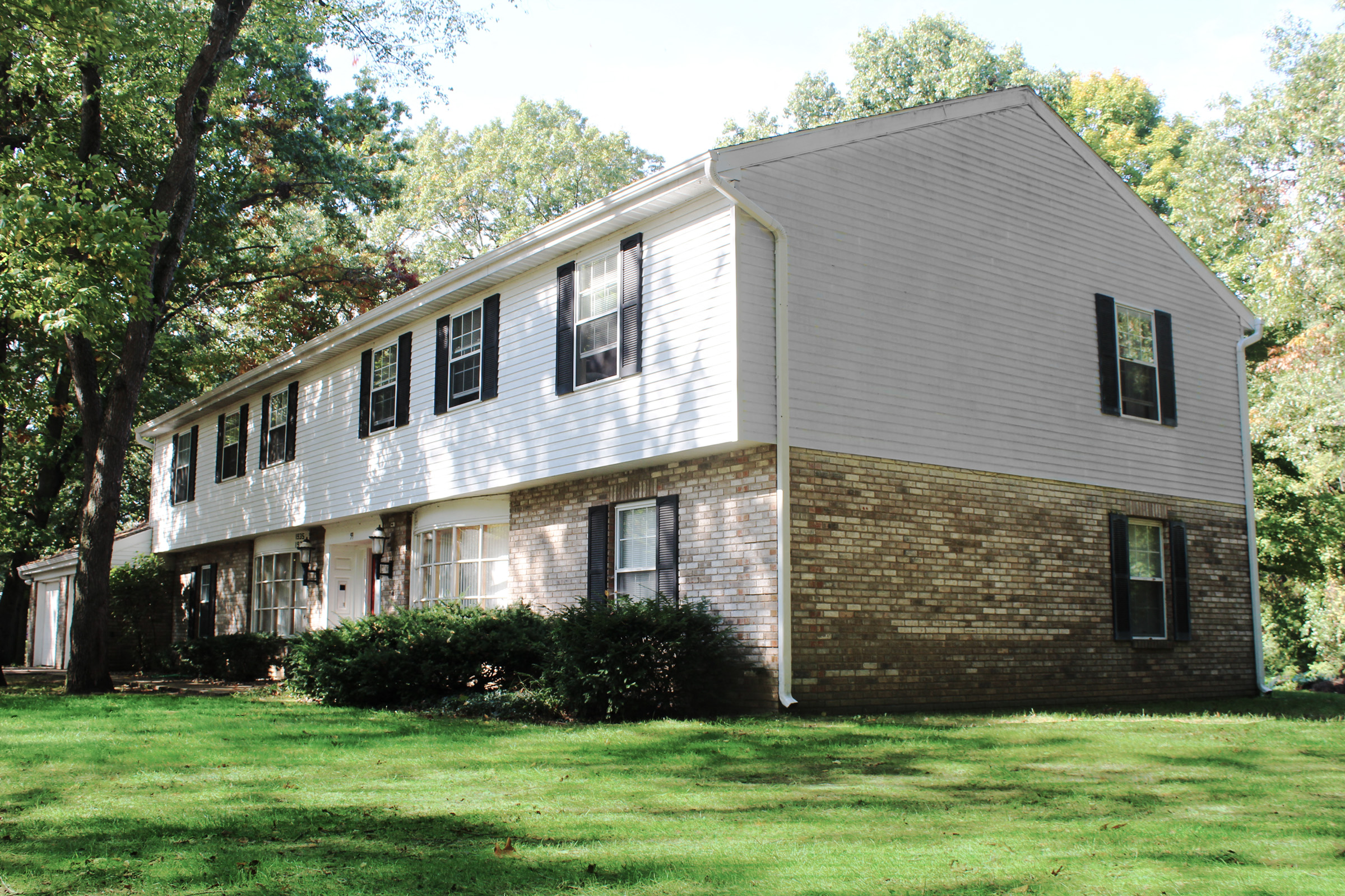 the side of a white house with a lawn and trees