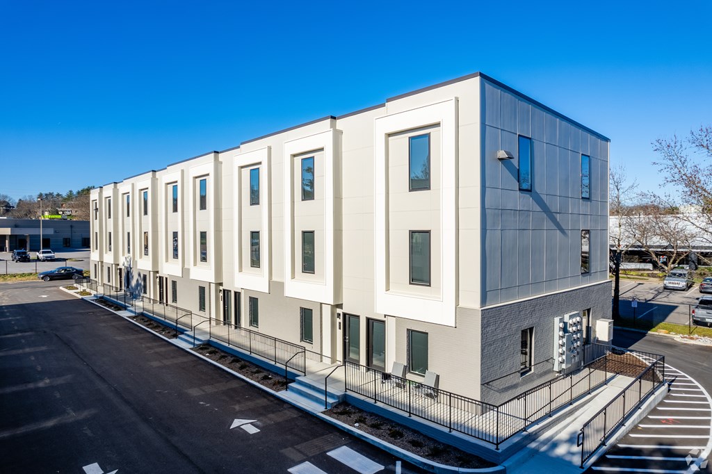 A modern building with a grey and white exterior and a parking lot in front.