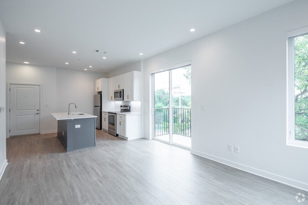 an empty living room with a kitchen and a balcony