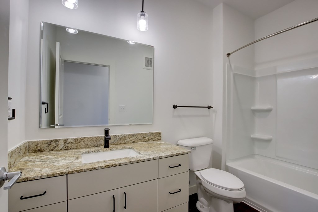 A bathroom with a marble countertop and white fixtures.