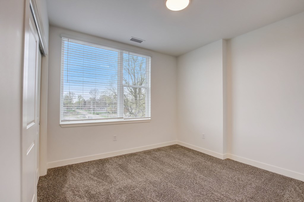 A room with a carpeted floor and a window with blinds.