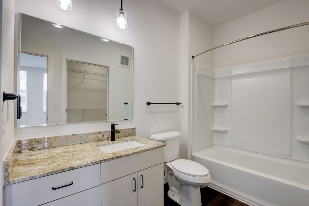 A white bathroom with a marble countertop and a large mirror.