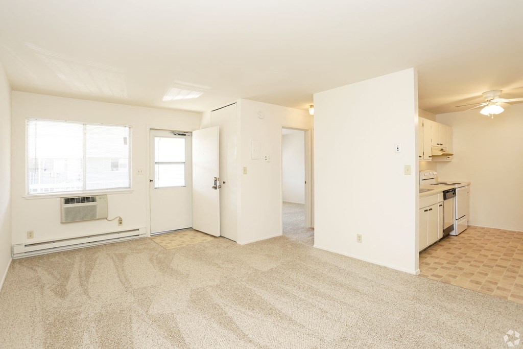 the living room and kitchen of an apartment with white walls and flooring