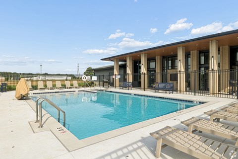 A pool with sun loungers and a building in the background.