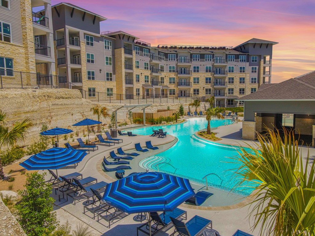 a resort style swimming pool with blue and white umbrellas and lounge chairs