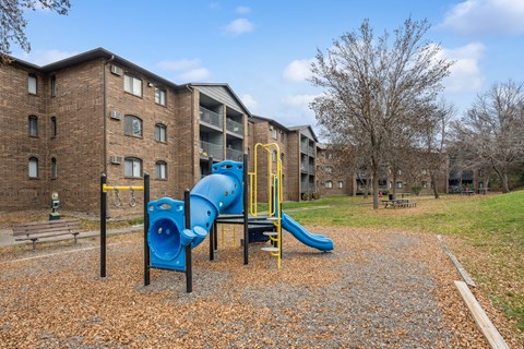A playground with a blue slide and yellow railing in front of a brick building.