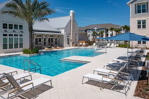 a large swimming pool with lounge chairs and a building in the background