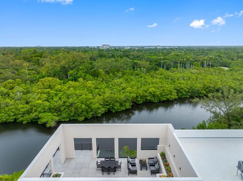 A balcony overlooks a lush green forest and a body of water.
