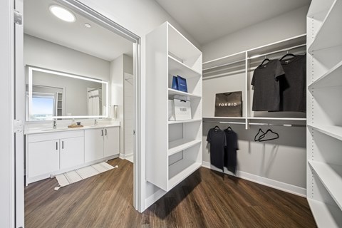 A walk in closet with a mirror and clothes hanging.