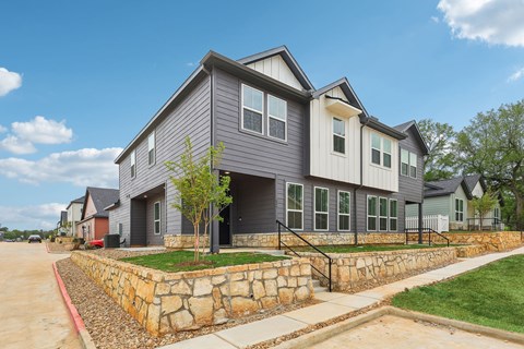 A modern house with a grey and white exterior and a stone wall in front.