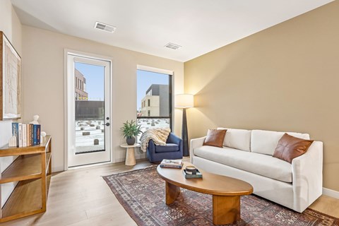 A living room with a white couch, a wooden coffee table, and a large window with a view of the outside.