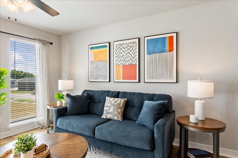 A living room with a blue couch and three framed artworks on the wall.